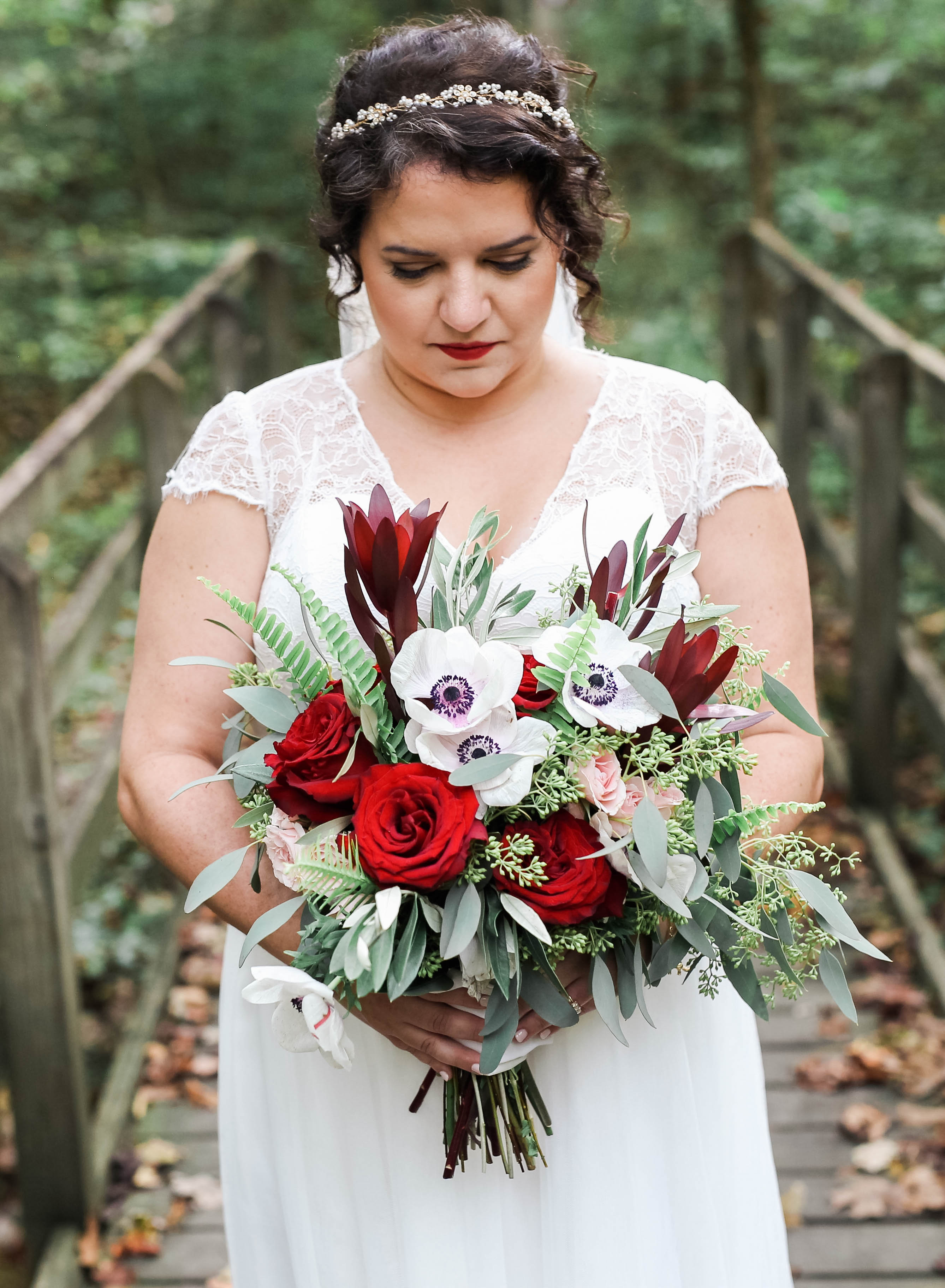 Bride holding a red and white woodland bouquet on a bridge