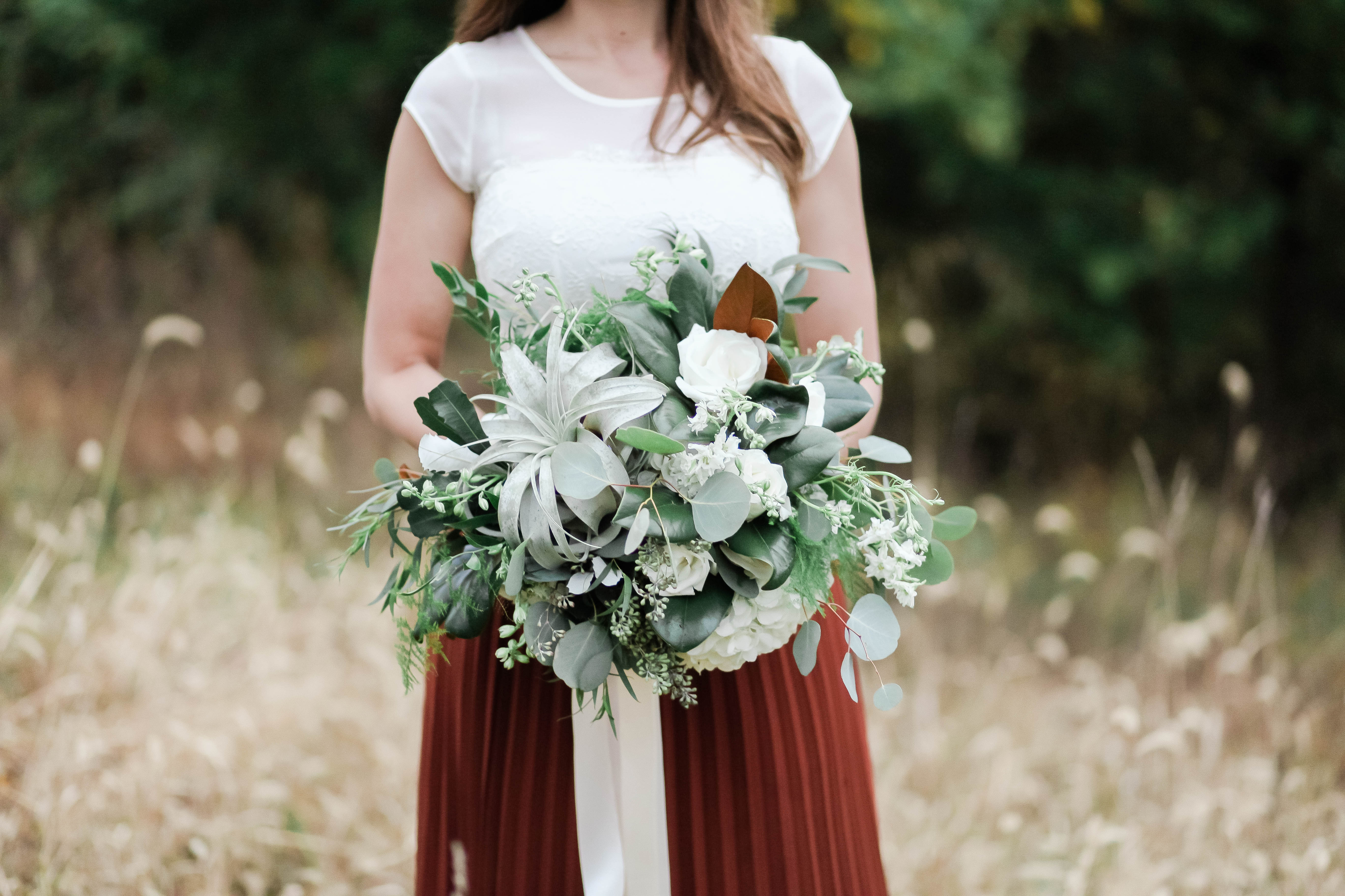 Bride holding a white and green bouquet in a golden field